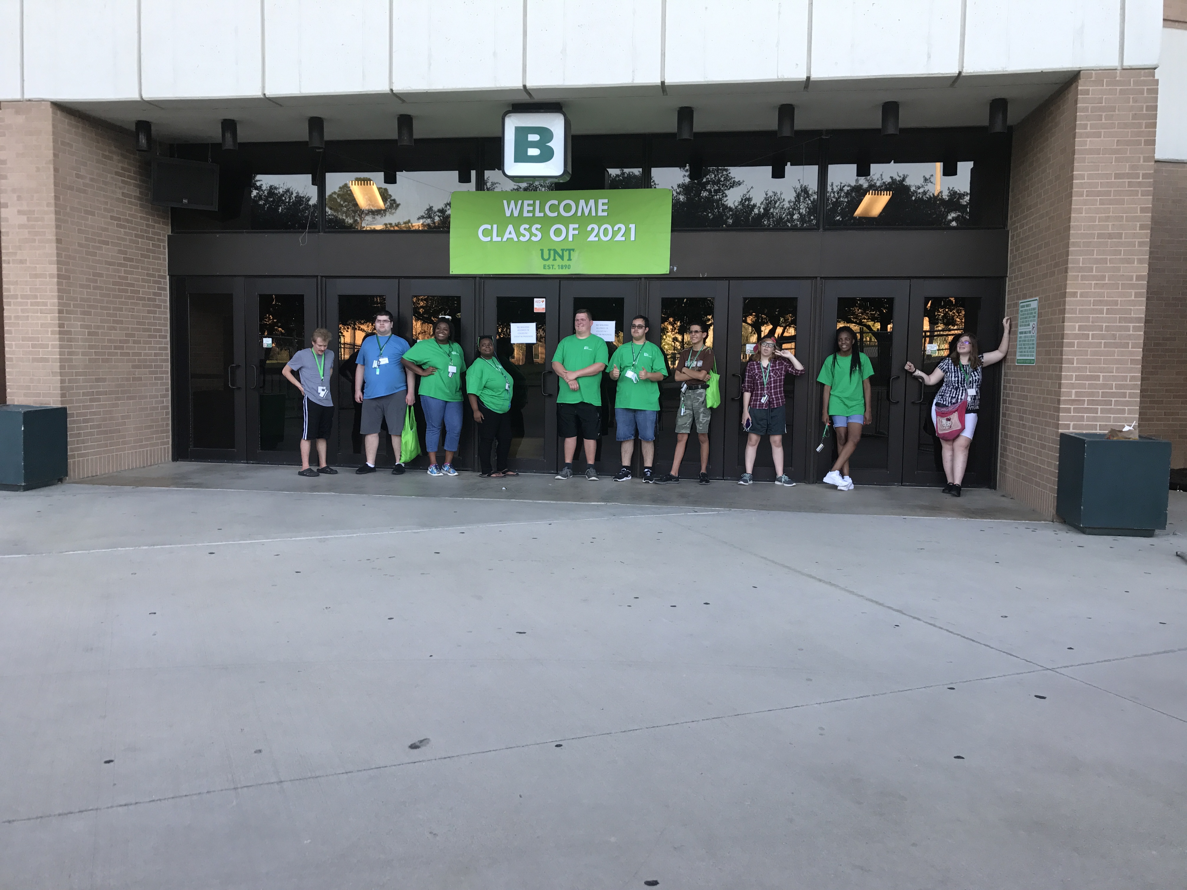 Group of participants in front of UNT Coliseum. Participants are standing by the glass doors, smiling and waving.