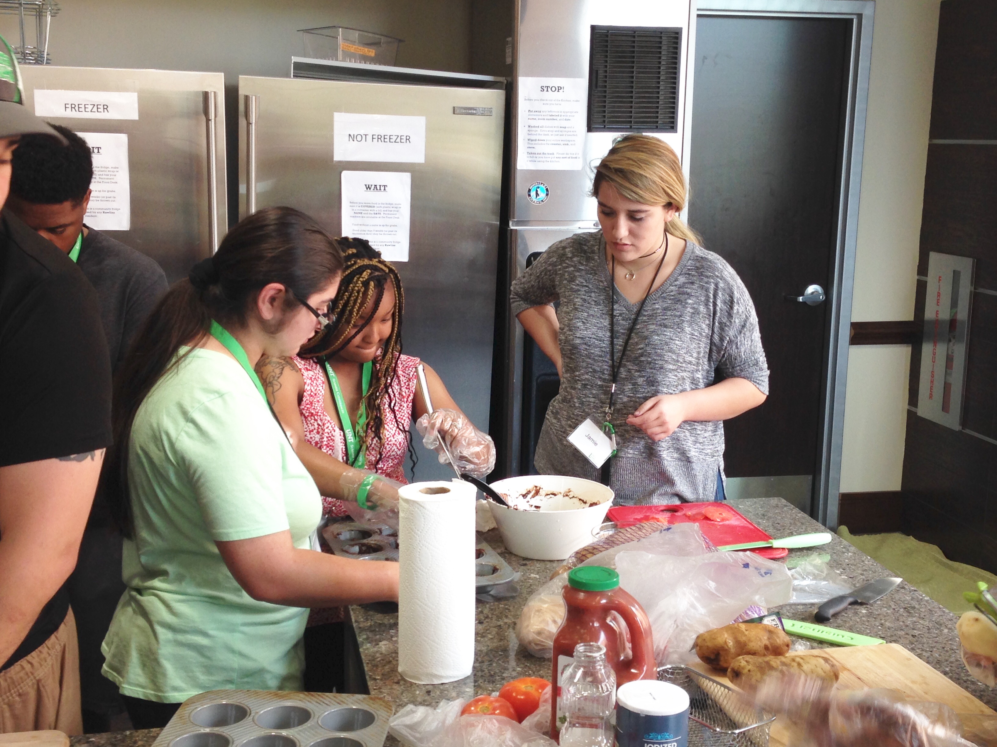 One staff and two participants preparing food in a mixing bowl.